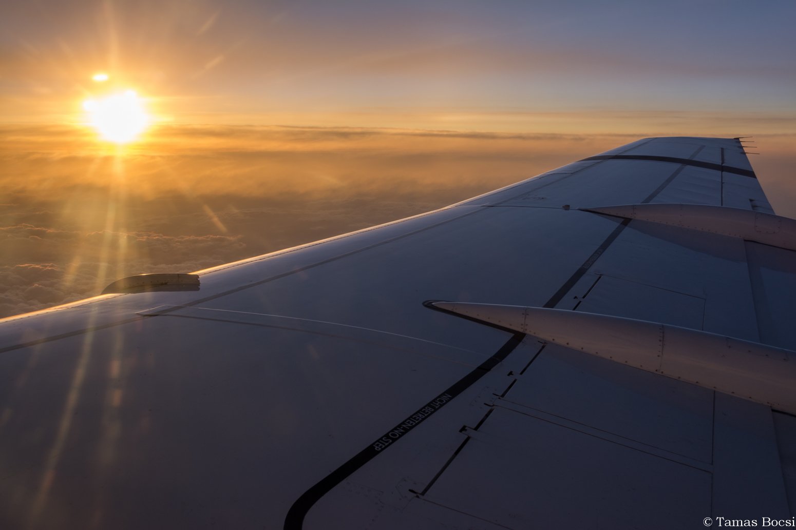 View from an airplane window showing a wing and a sunset sky with clouds.