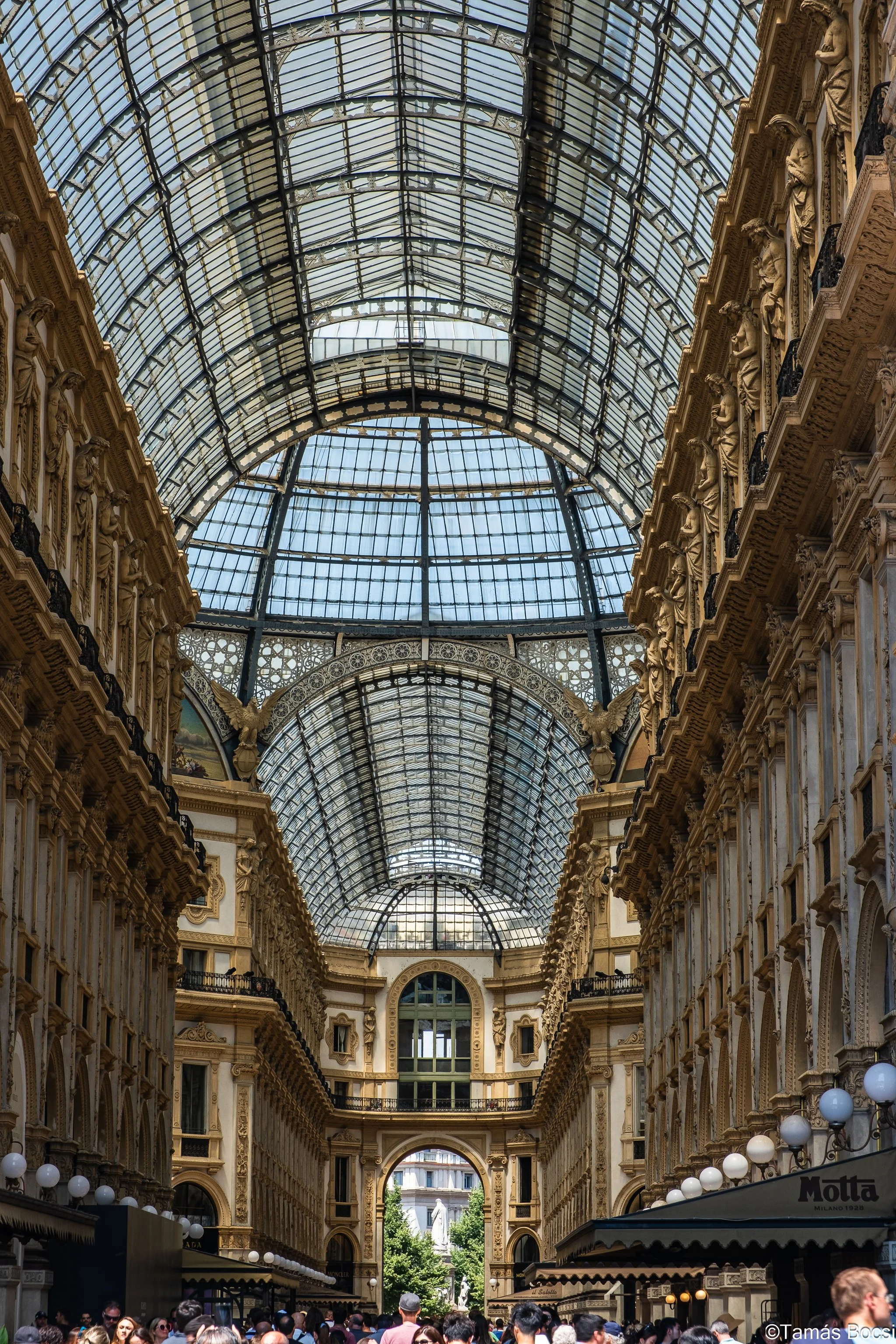 A crowded indoor shopping arcade with ornate architecture and a glass-domed ceiling.
