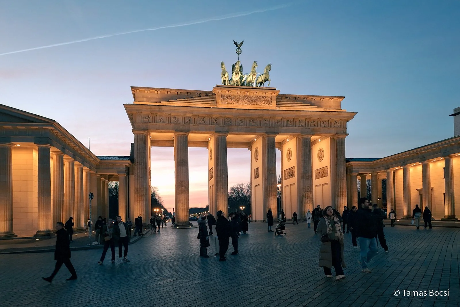 Brandenburg Gate at sunset with people walking around it.