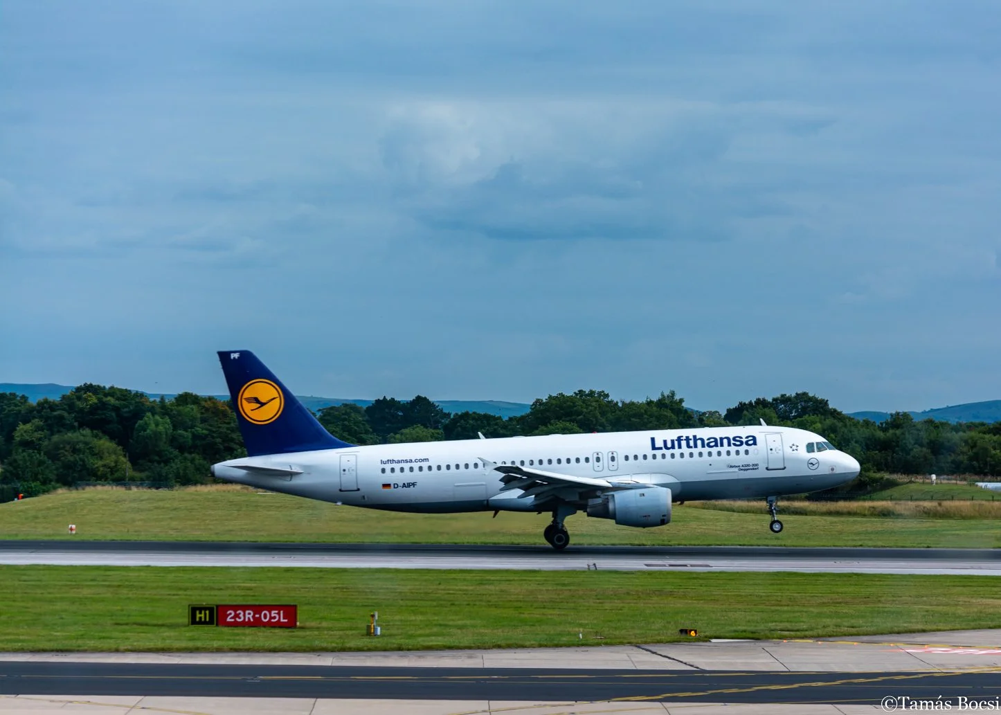 Lufthansa airplane on runway during daytime with trees and blue sky in the background.