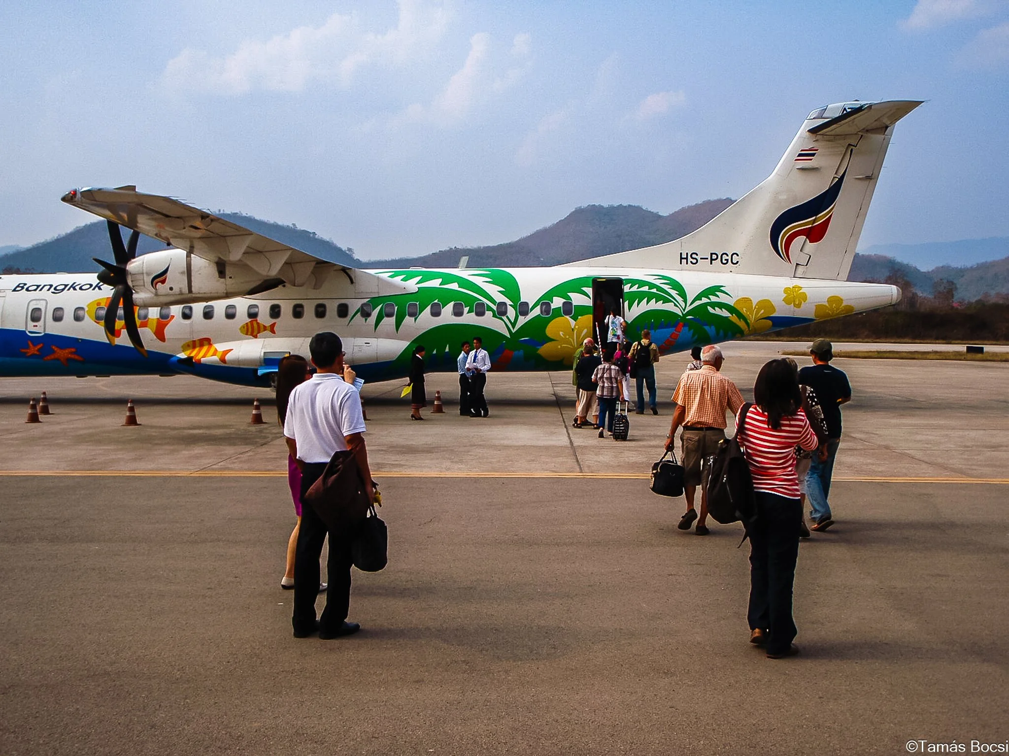 Passengers walking towards a colorful airplane with tropical-themed artwork on the tarmac.