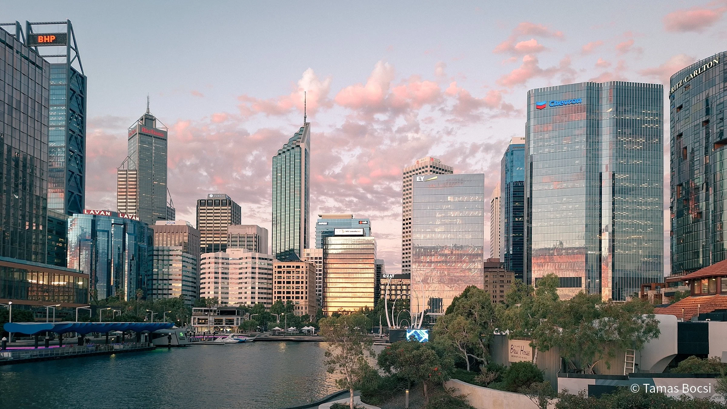 City skyline with modern skyscrapers view from a waterfront park at sunset, reflecting in the river.