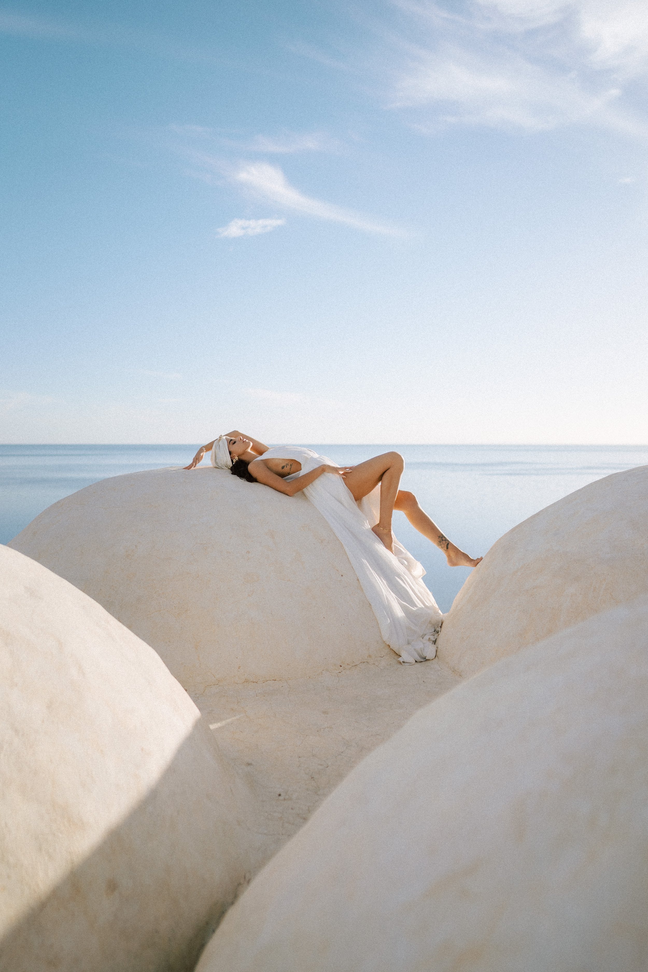 Woman in white dress lounging on large white roof by the sea under the blue sky of djerba.
