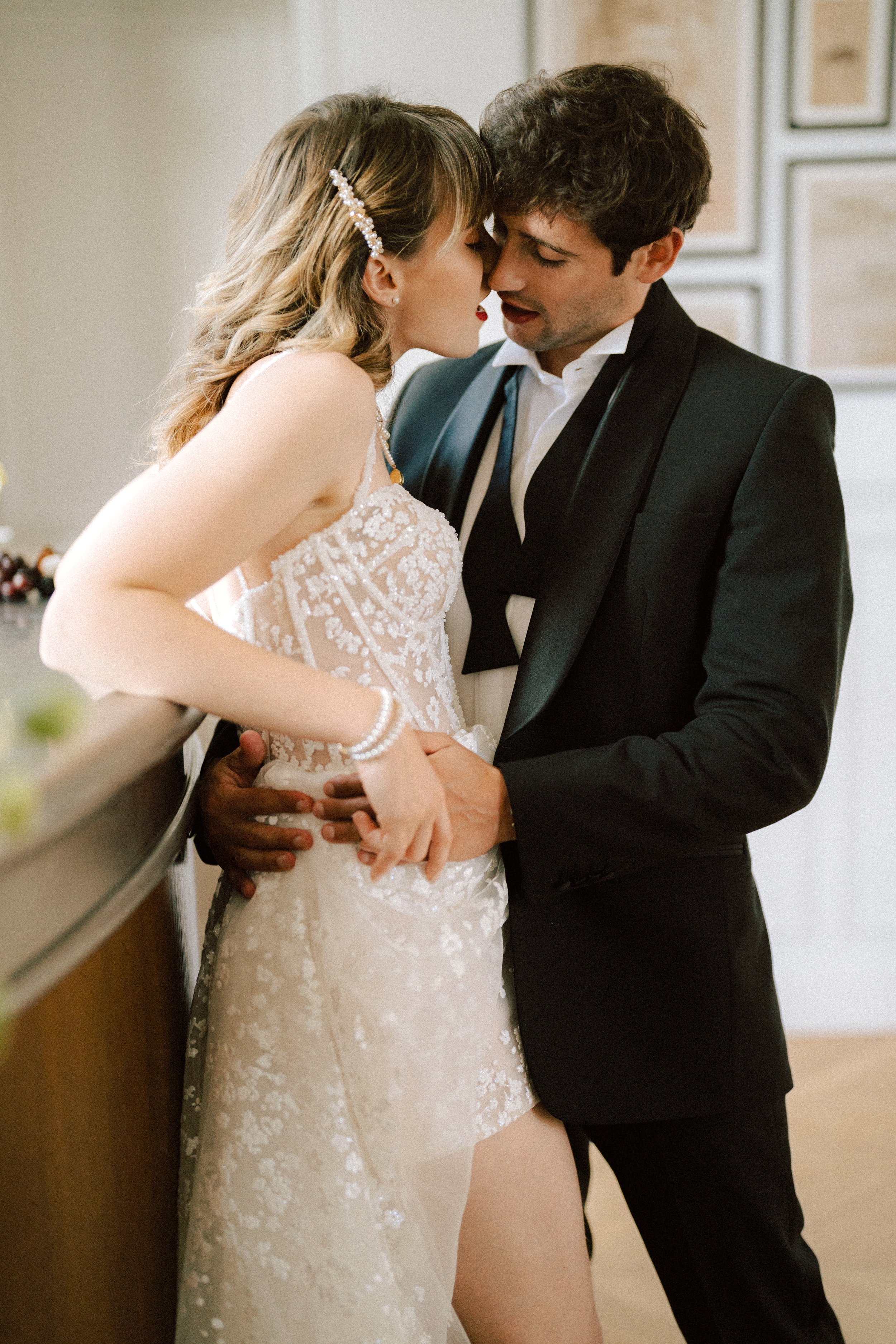 A couple embracing closely, woman in a white lace Alberto Palatchi dress, man in a black suit.