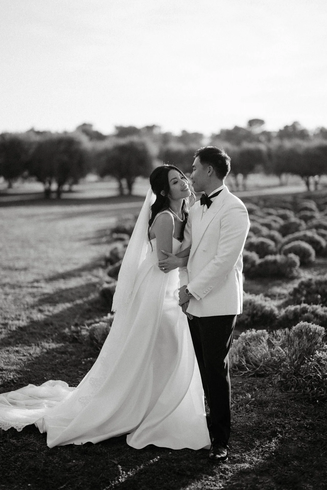A bride and groom share a romantic moment outdoors, with the bride in a white gown and the groom in a white tuxedo jacket at mas de la rose, provence.