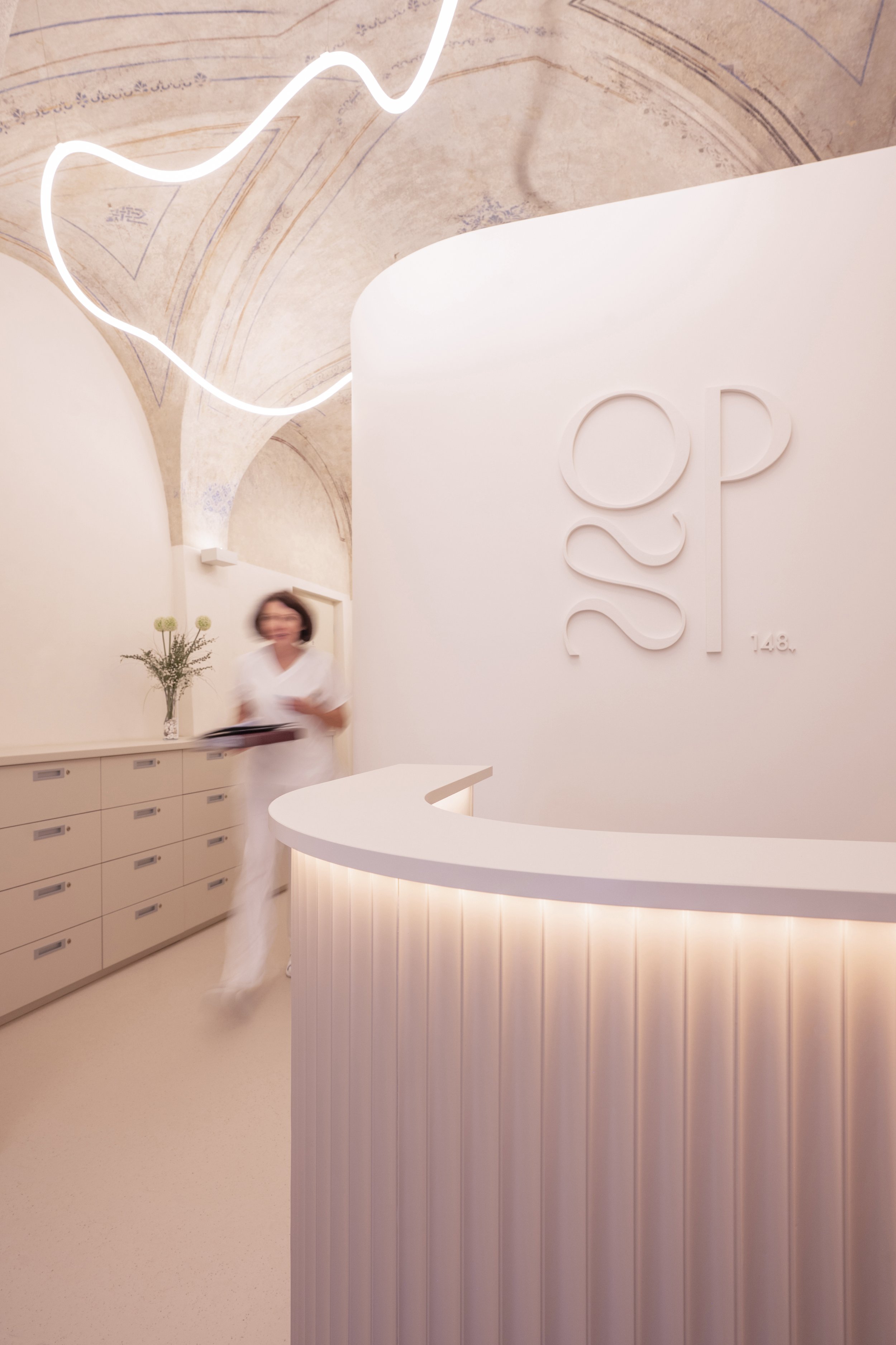 Reception area featuring the " Ordinace Pod Štítem " logo and an illuminated snake beneath the vaulted ceiling