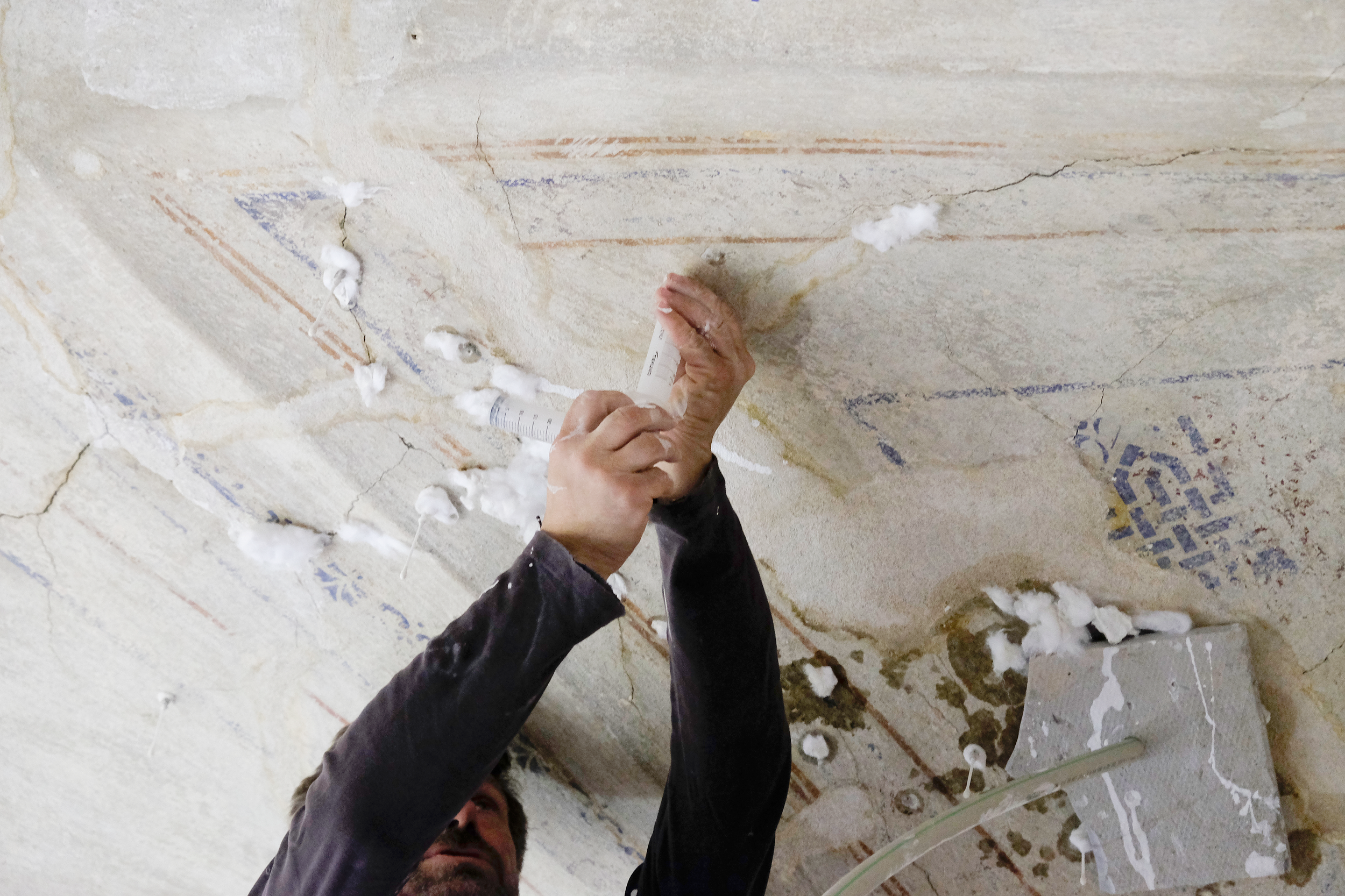 A restorer is injecting loose historic plaster into the vault