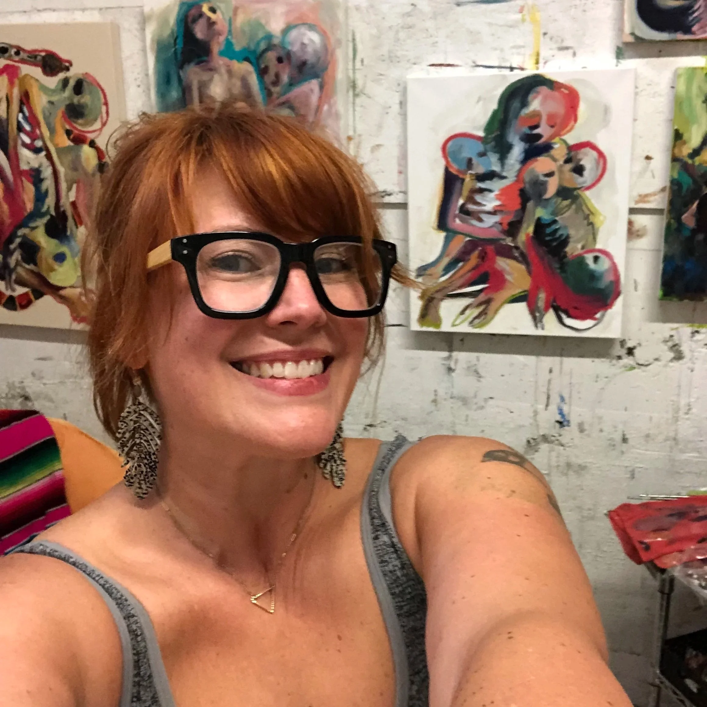 A woman with short red hair, black glasses, and earrings, smiling in front of colorful abstract paintings, with the text 'Beginning Oil Painting' at the top.