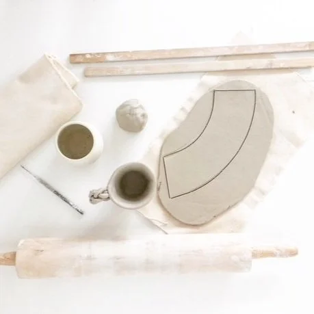 Pottery tools, clay, and a sculpted clay piece on a white workspace.