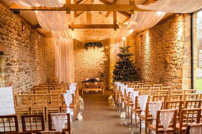 Wedding reception hall with decorated chairs, a flower arrangement on the table, and flower petals scattered on the wooden floor.