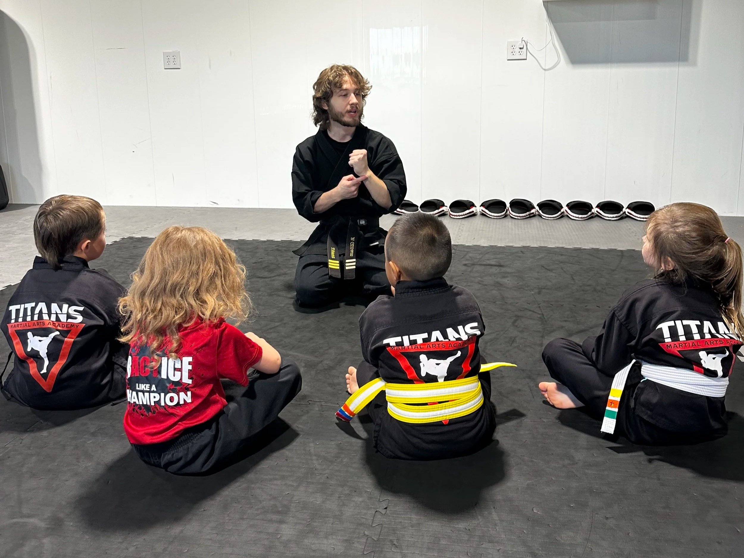 Martial arts instructor demonstrating a technique to children seated on training mats at a Titans Martial Arts Academy class