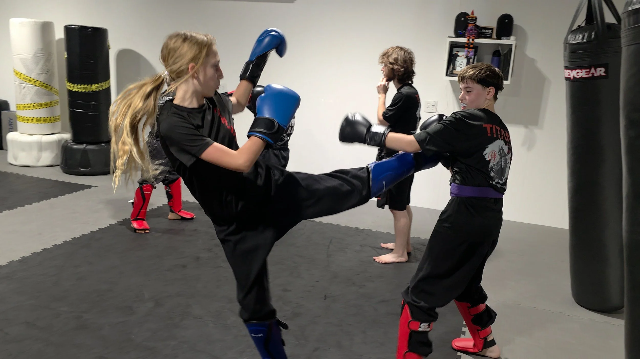 Martial arts students practicing a kicking drill in a training gym with punching bags.