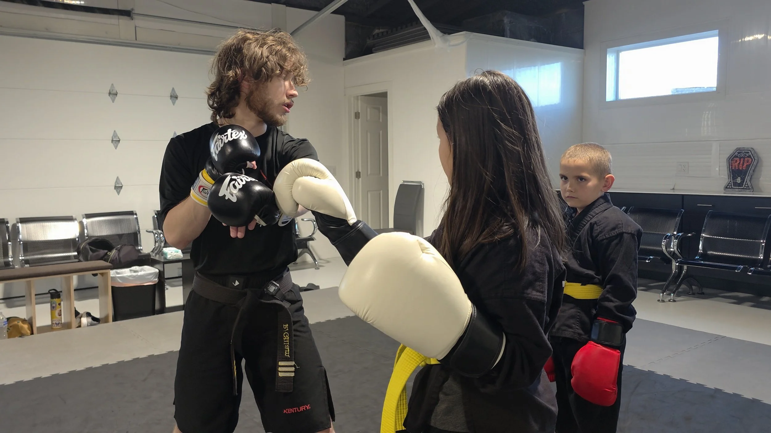 Martial arts instructor holding focus mitts while training a woman and child in a dojo.