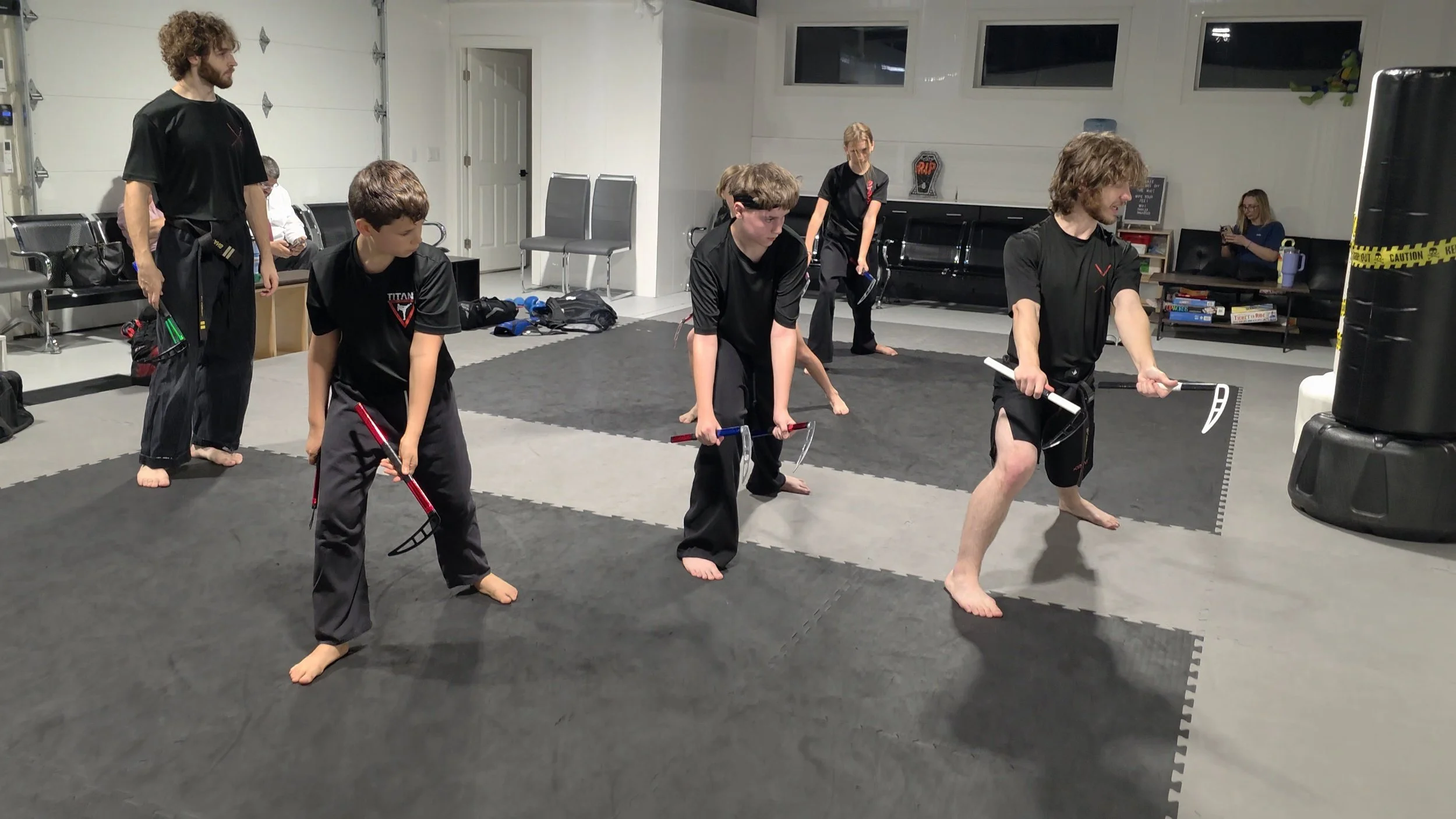 Martial arts students practicing with padded weapons on a training mat in a garage gym