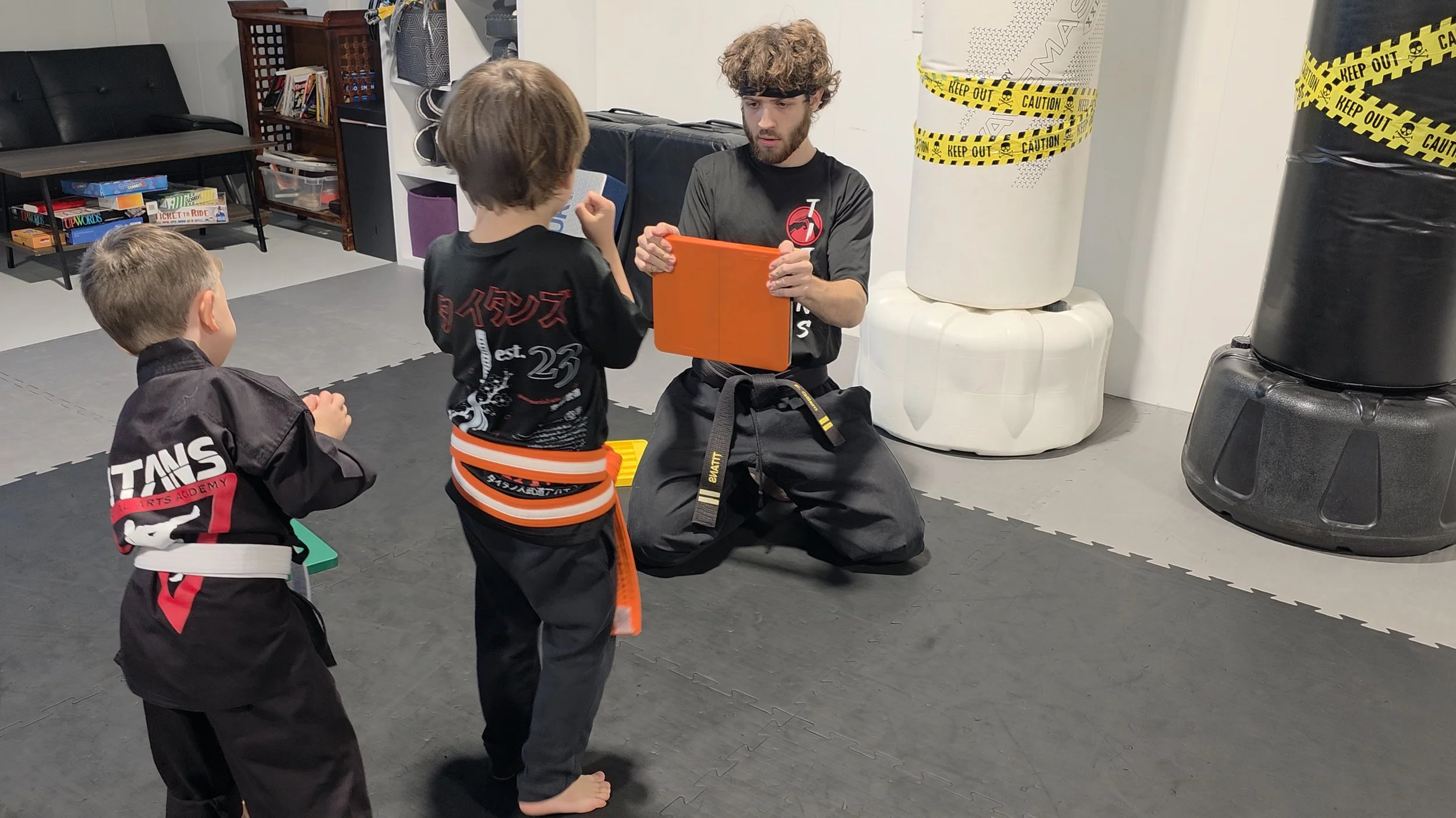Martial arts instructor teaching two children in a dojo while holding an orange training shield