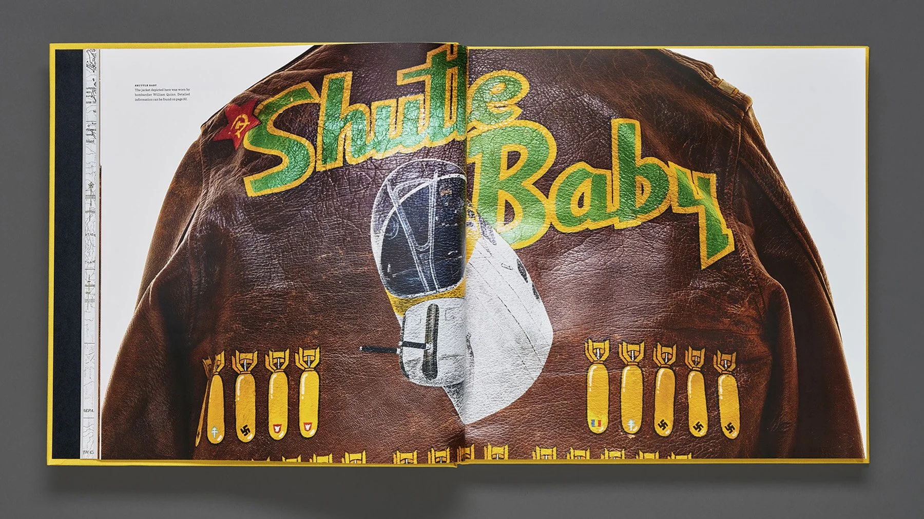A leather jacket with rainbow-colored text saying "Shuttle Baby" and cartoon-like bombs with swastikas, crosses, and other symbols on a WWII leather A-2 flight jacket.
