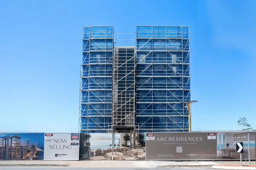 Building under construction with scaffolding, surrounded by fencing and advertising for Arc Residences.