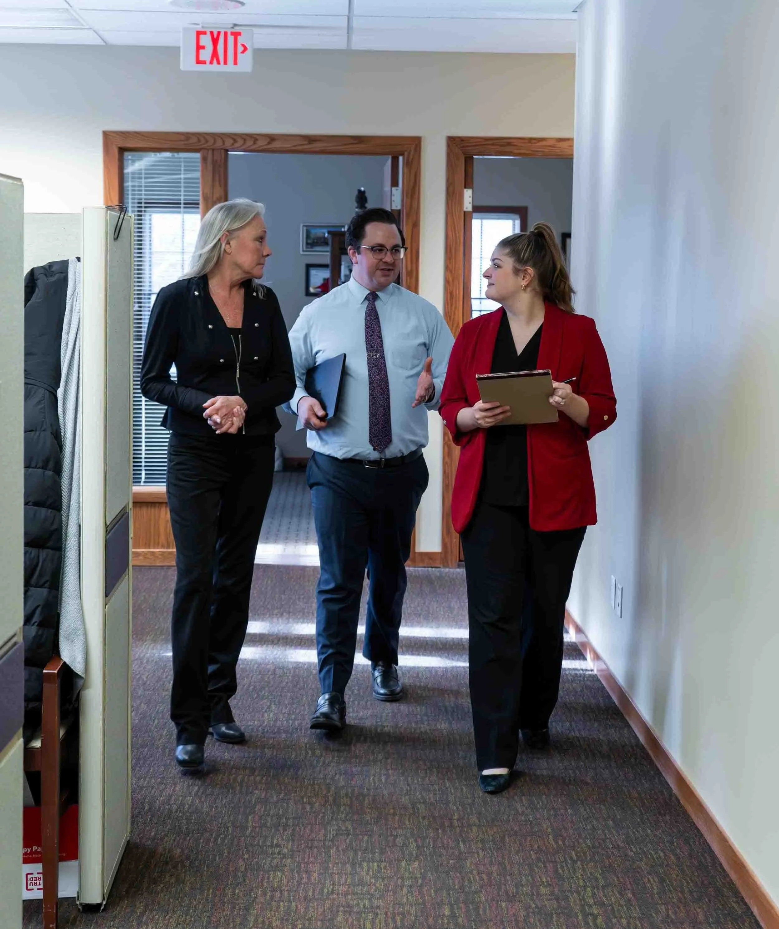 Three business professionals, including a family law attorney in Michigan, walk down an office hallway discussing legal strategies.