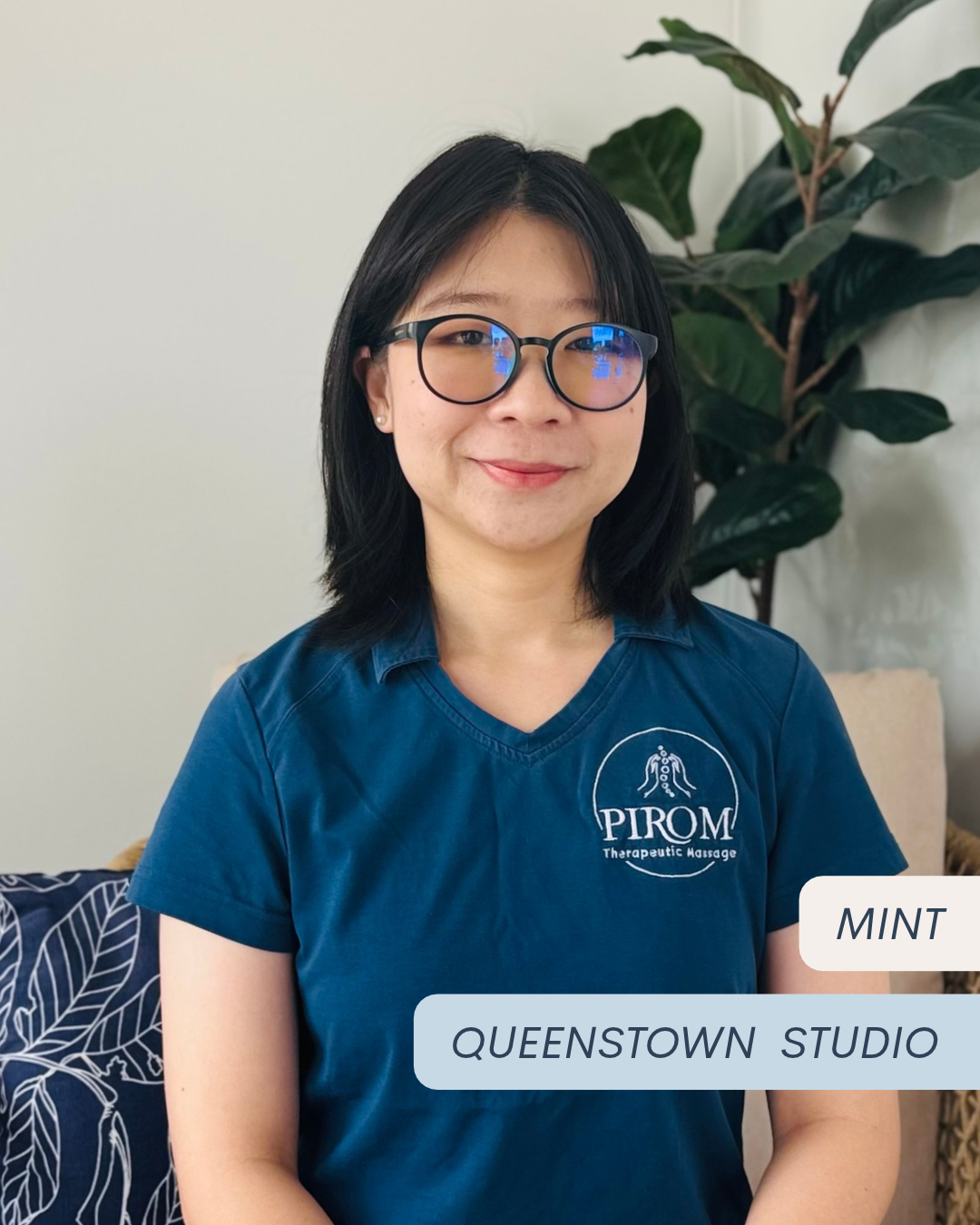 Mint Nawaporn, Thai-qualified physiotherapist and massage therapist at Pirom Therapeutic Massage in Frankton, Queenstown, wearing a navy Pirom uniform and seated in the studio reception area