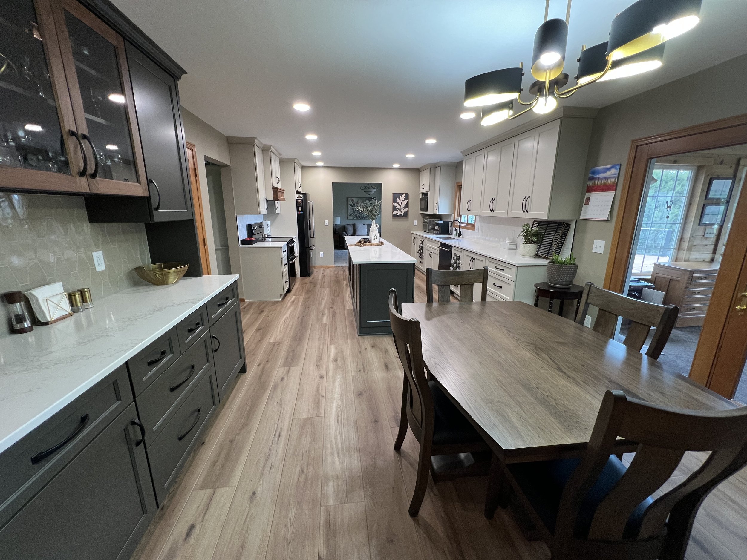 A spacious kitchen with light-colored cabinets, a kitchen island, wooden floors, a dining table with chairs, and various appliances including a stove, microwave, and refrigerator.