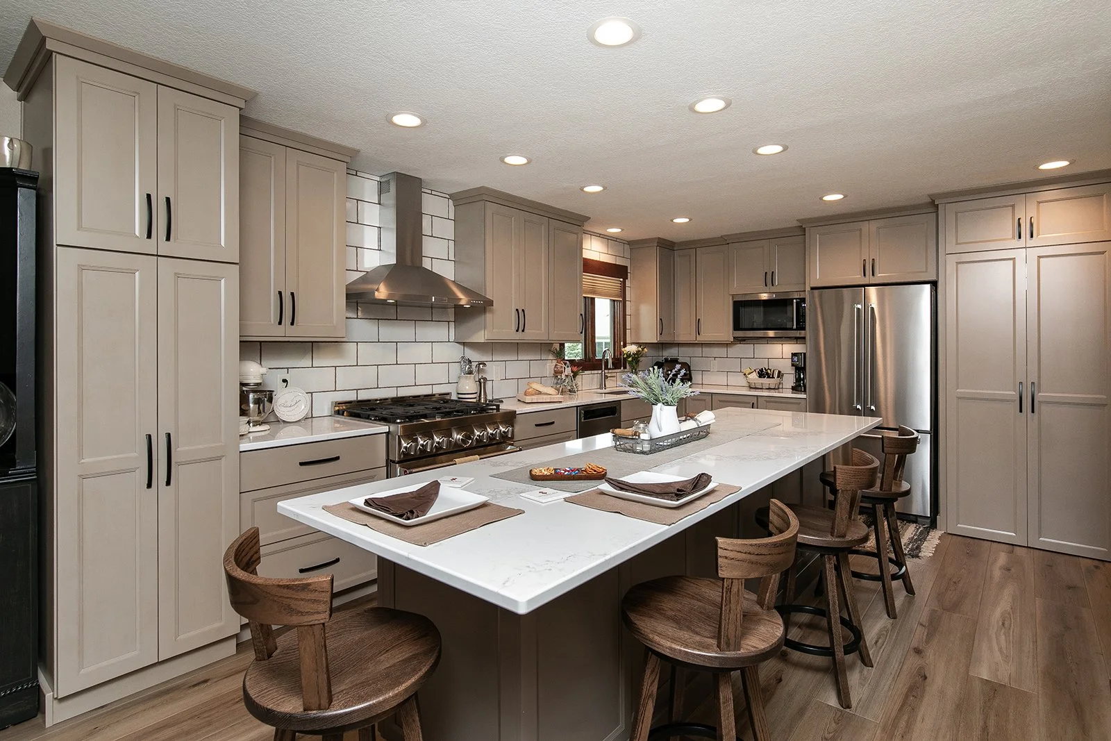 Modern kitchen with beige cabinets, white marble-look island, stainless steel refrigerator, and stove, with wooden chairs around the island.
