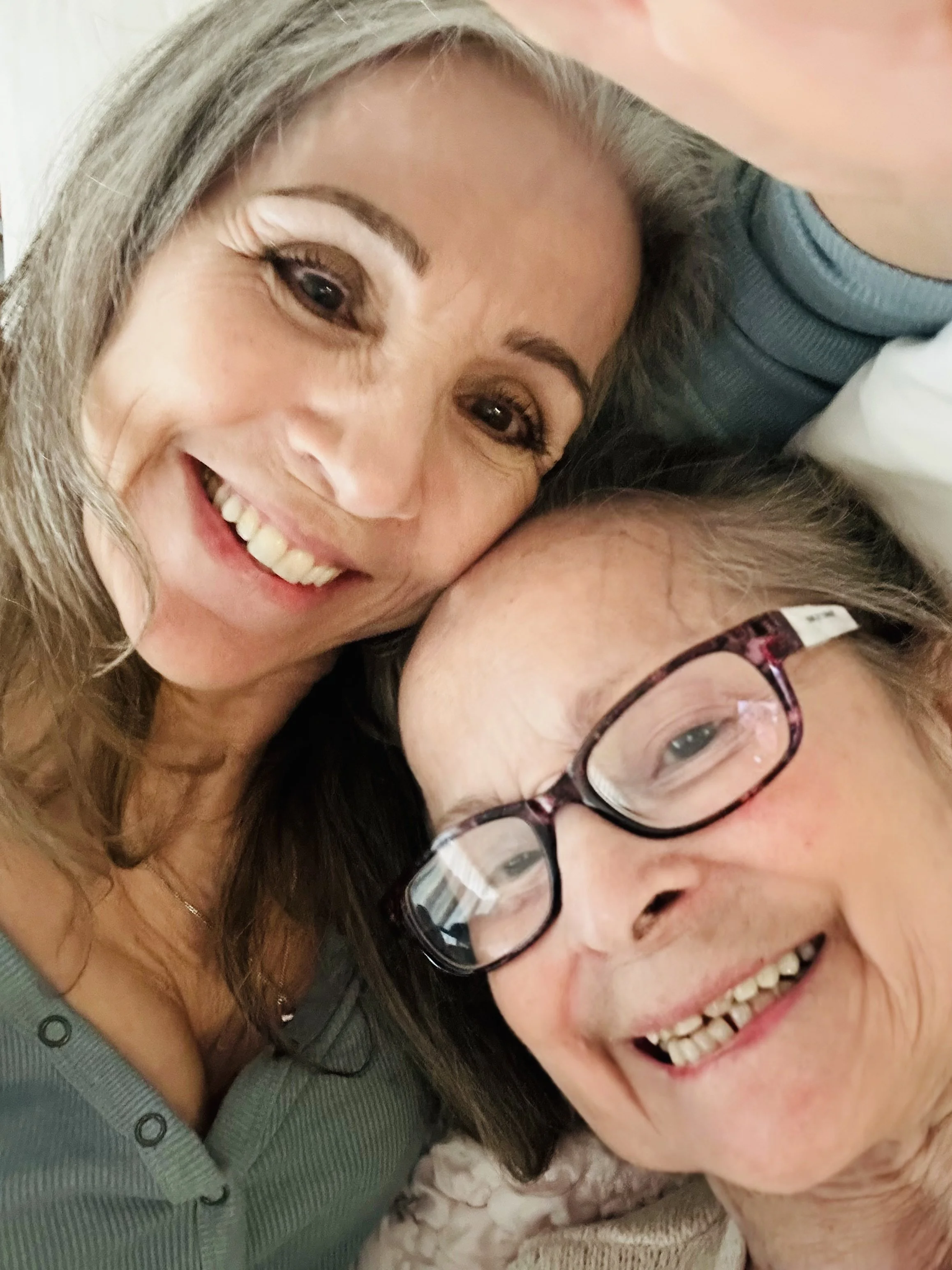 Two women smiling and lying close together, showing their faces and expressions in a close-up photo.