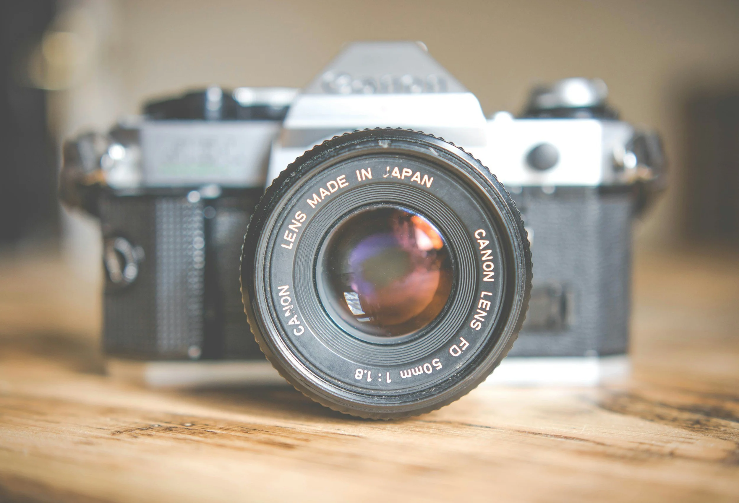 An old camera with a Canon lens in front, placed on a wooden surface.
