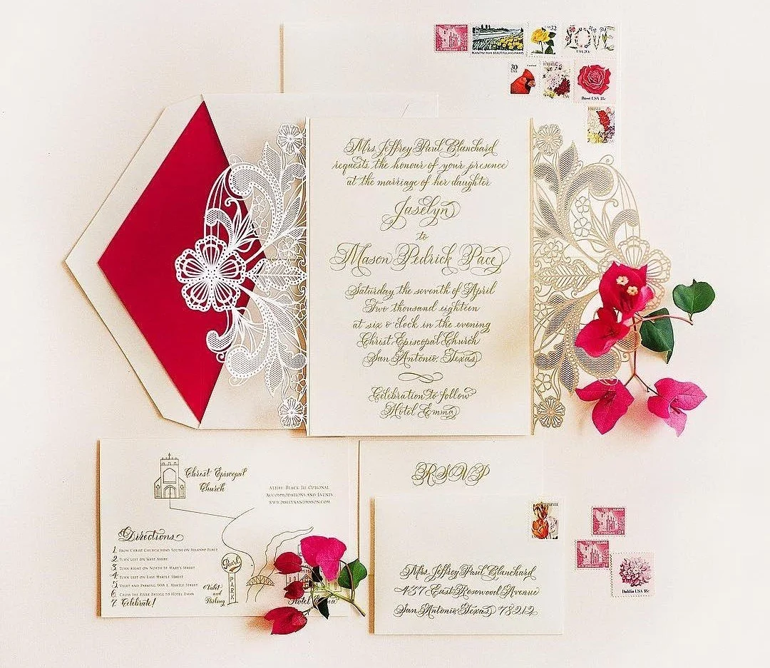 Wedding invitation set with gold and floral designs, pink flowers, and vintage stamps, arranged with an envelope and RSVP card.