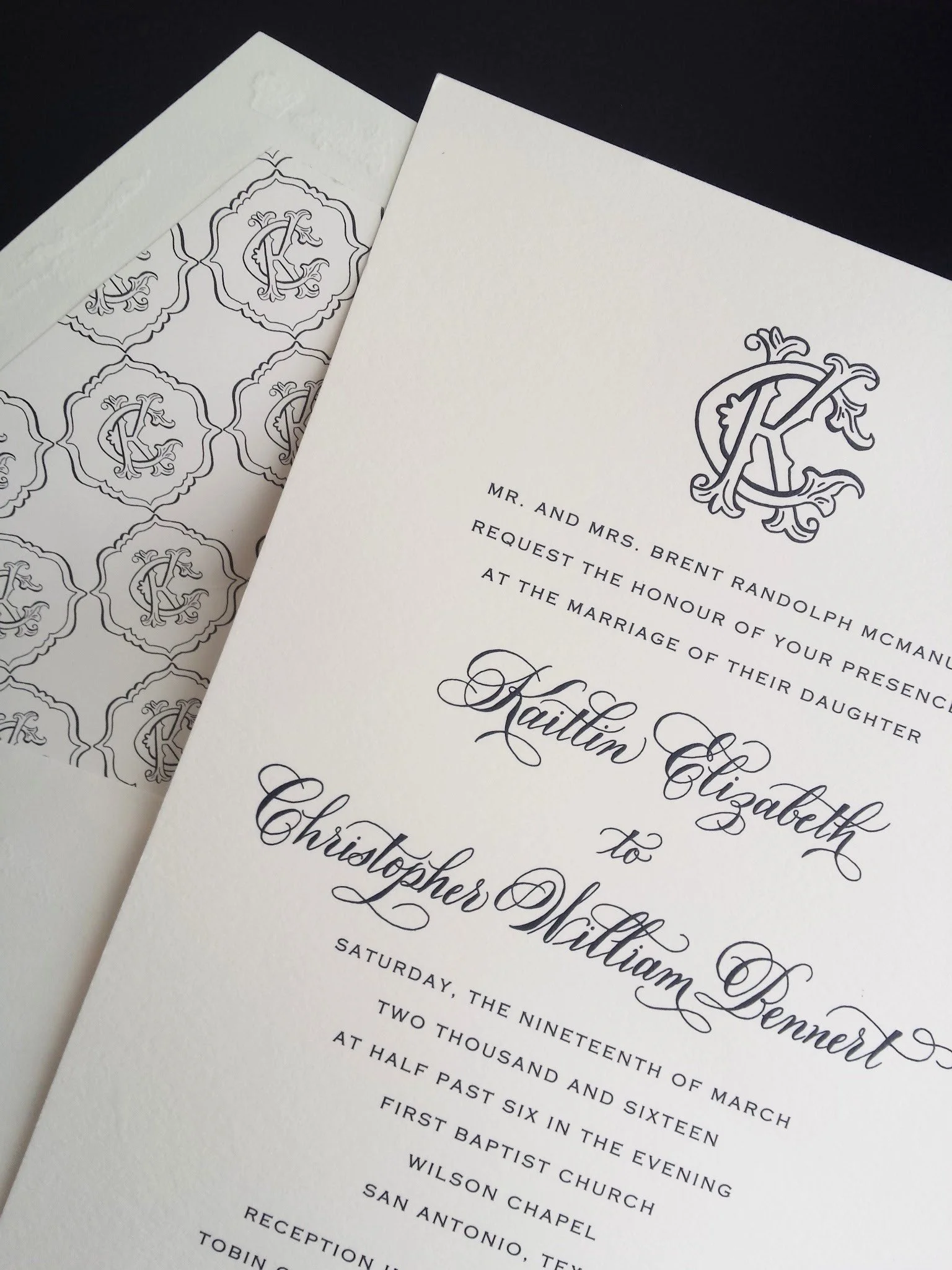 Wedding invitation with ornate monogram and elegant script, surrounded by matching patterned envelope liner.