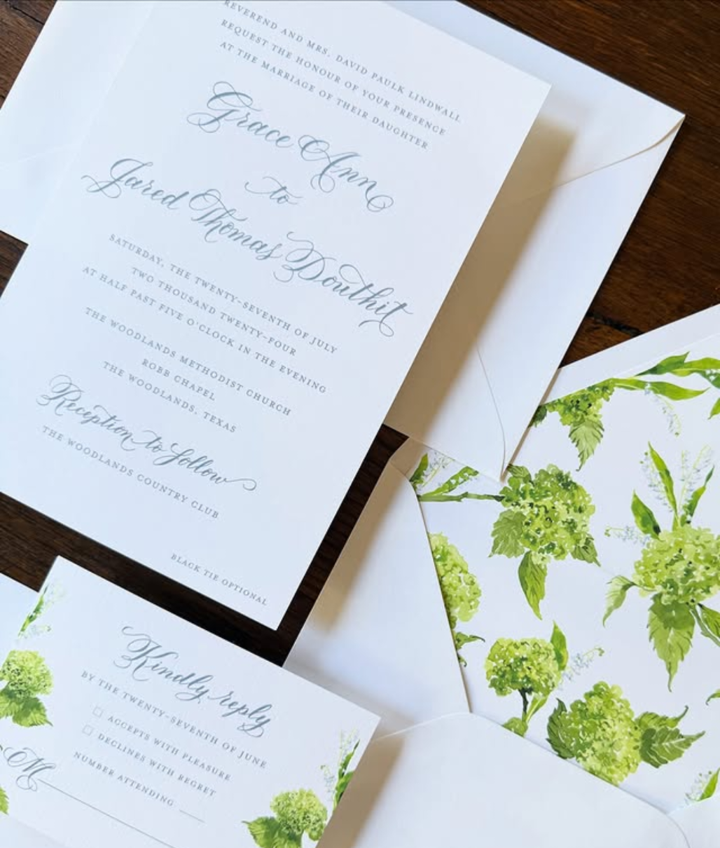 Wedding invitation in calligraphy with floral design and matching RSVP card on a wooden surface.