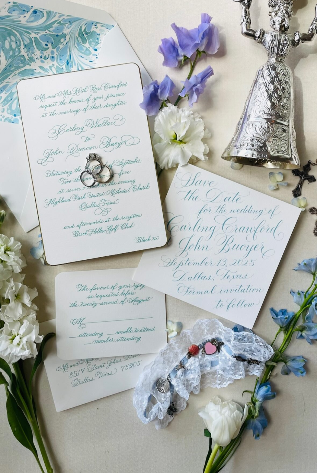 Wedding invitation suite with rings, flowers, a bell, and jewelry on a beige background.
