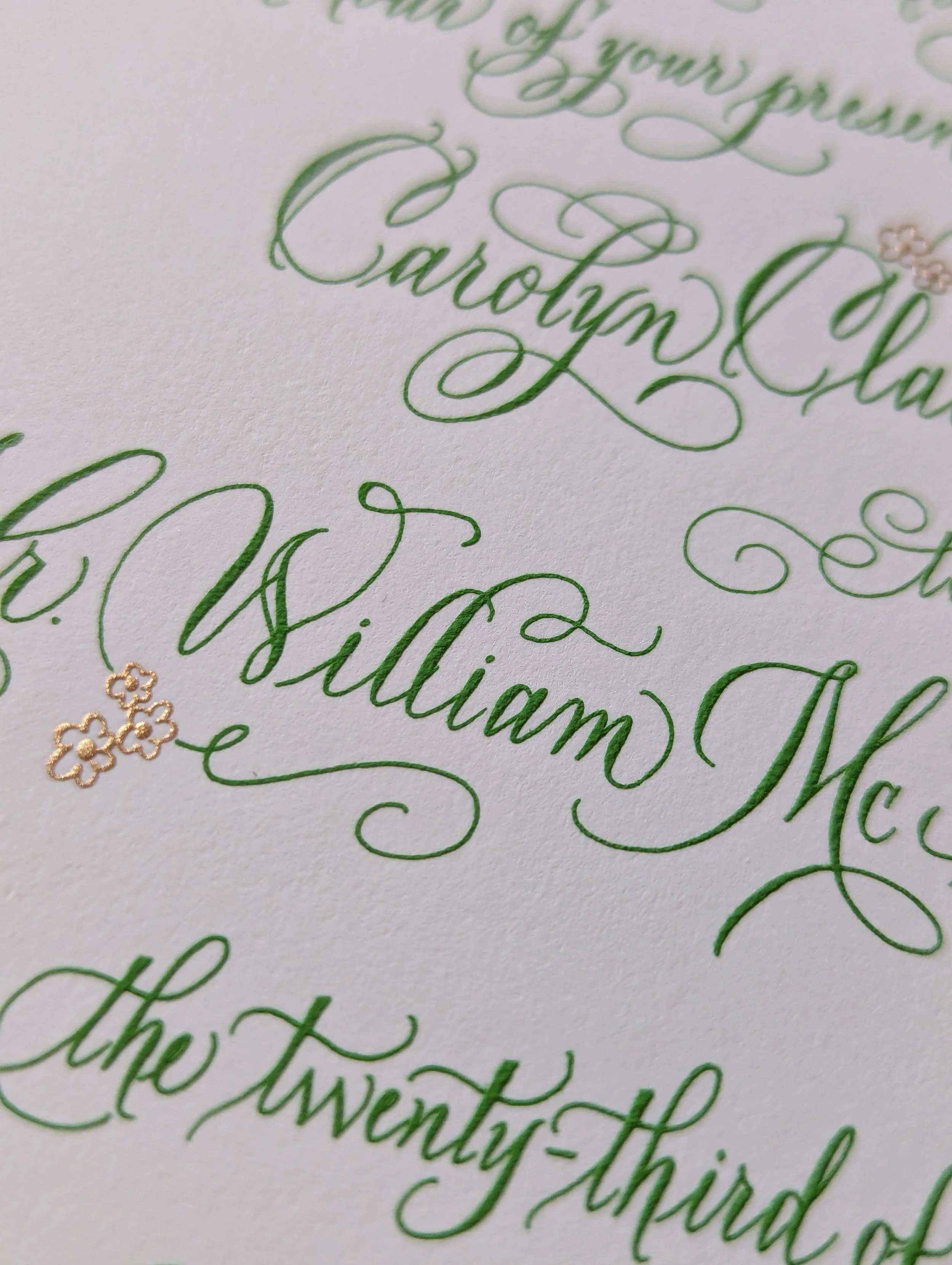 Close-up of elegant green calligraphy with small gold flower accents on textured white paper.