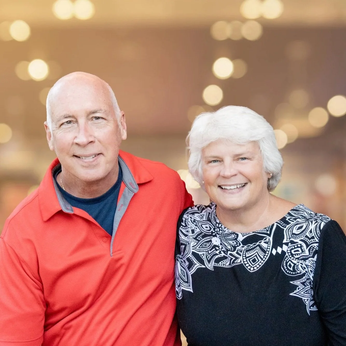 A smiling middle-aged man and woman standing in front of a brick wall, close together.