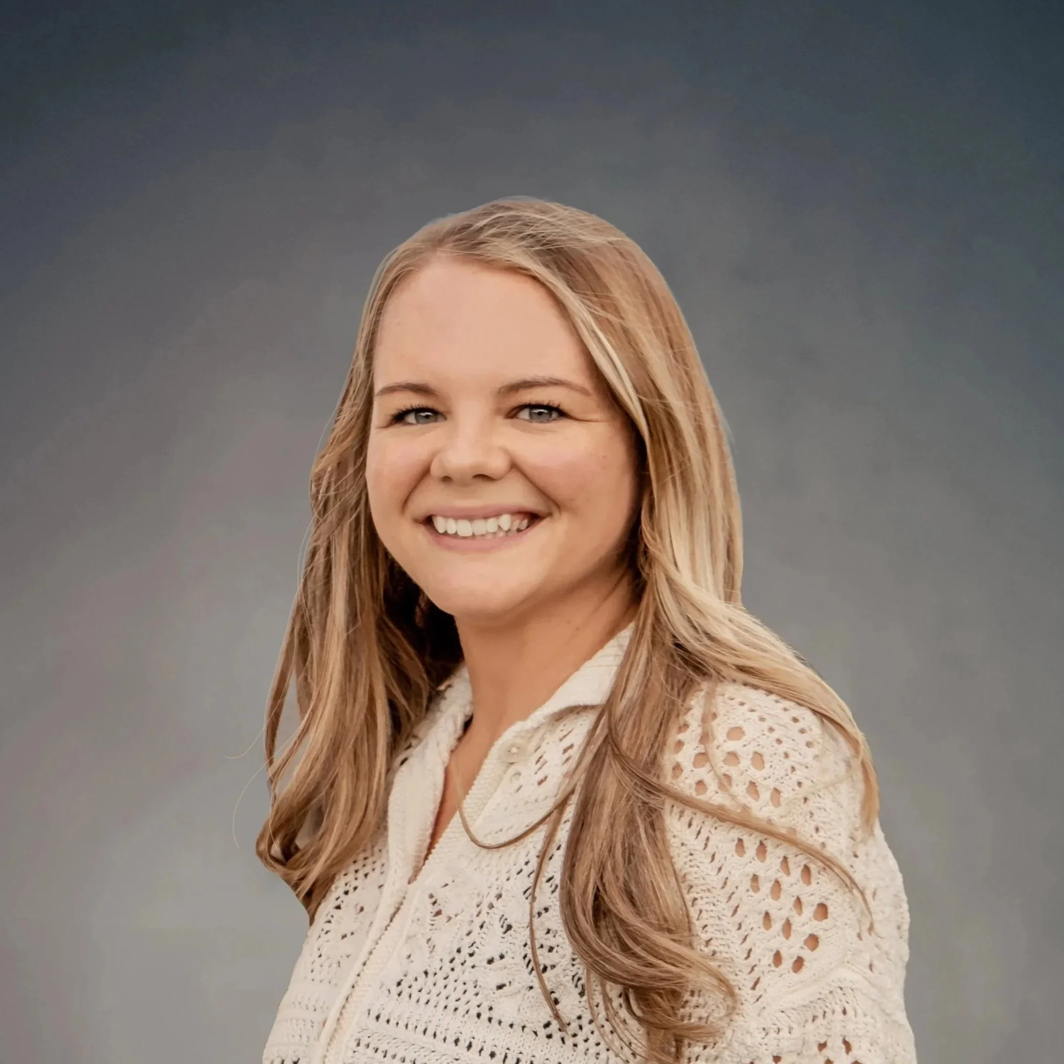 A young woman smiling with braces on her teeth, wearing a brown checked shirt over a black top, against a gradient background.
