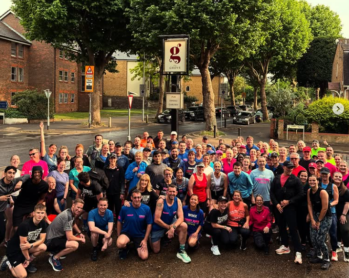 A large group of people gathered outside The Grove Surbiton pub, posing for a group photo after running event. A range of ages and backgrounds in Kingston.