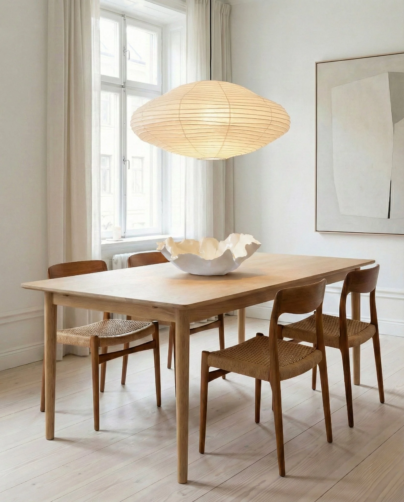 A dining room with a wooden table, four chairs, a large paper lantern hanging above, a white abstract sculpture in the center, white curtains, and a large abstract artwork on the wall.