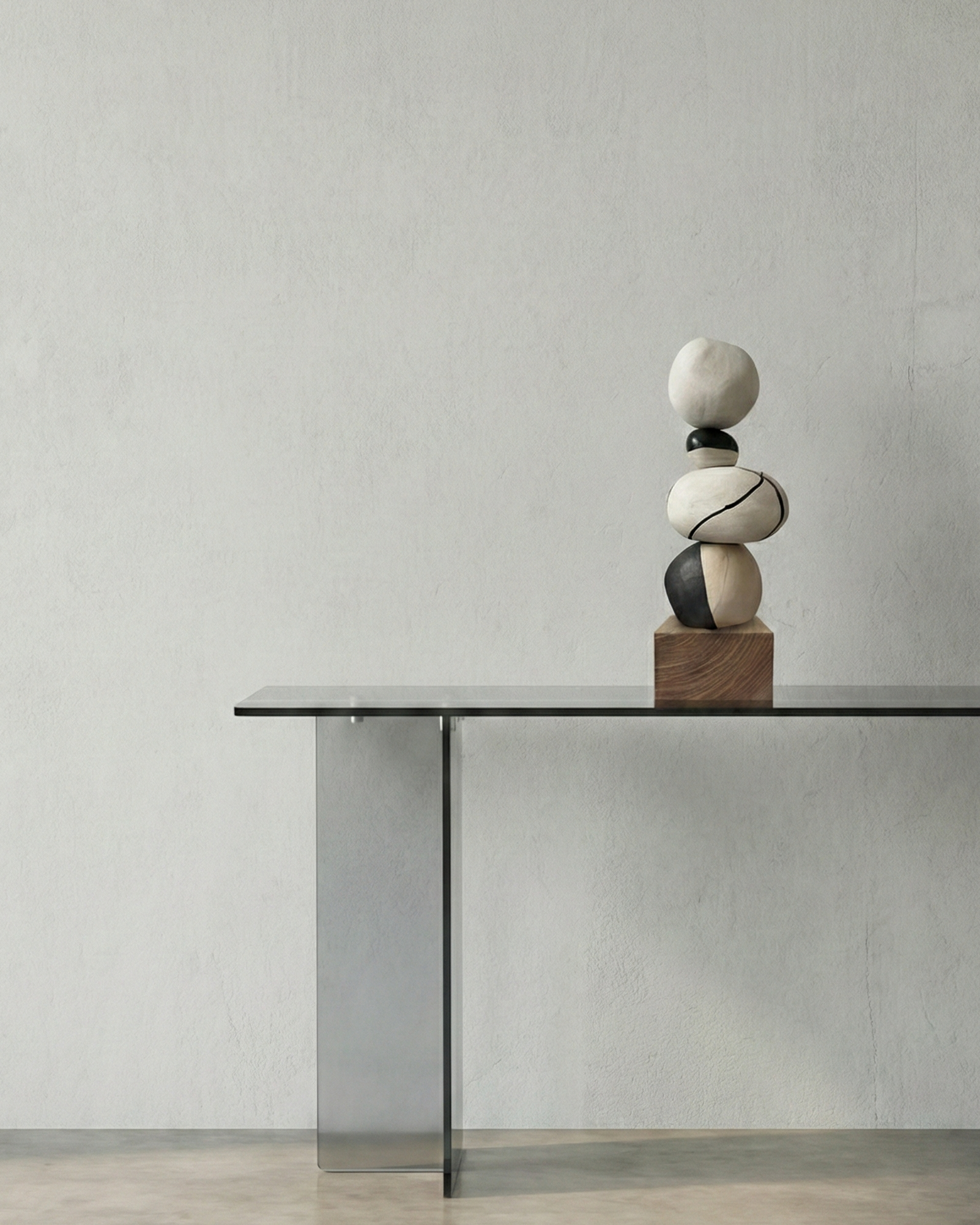 A minimalist interior with a sleek gray table with a metal support, featuring a wooden block with a stack of abstract, smooth, rounded stones in black, white, and gray tones.