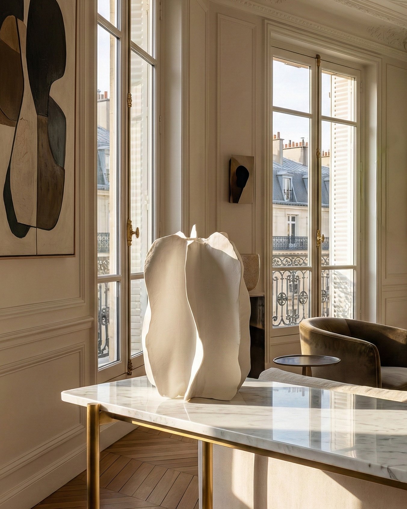 Elegant living room with large windows, a marble-topped table, abstract sculptures, and modern artwork.