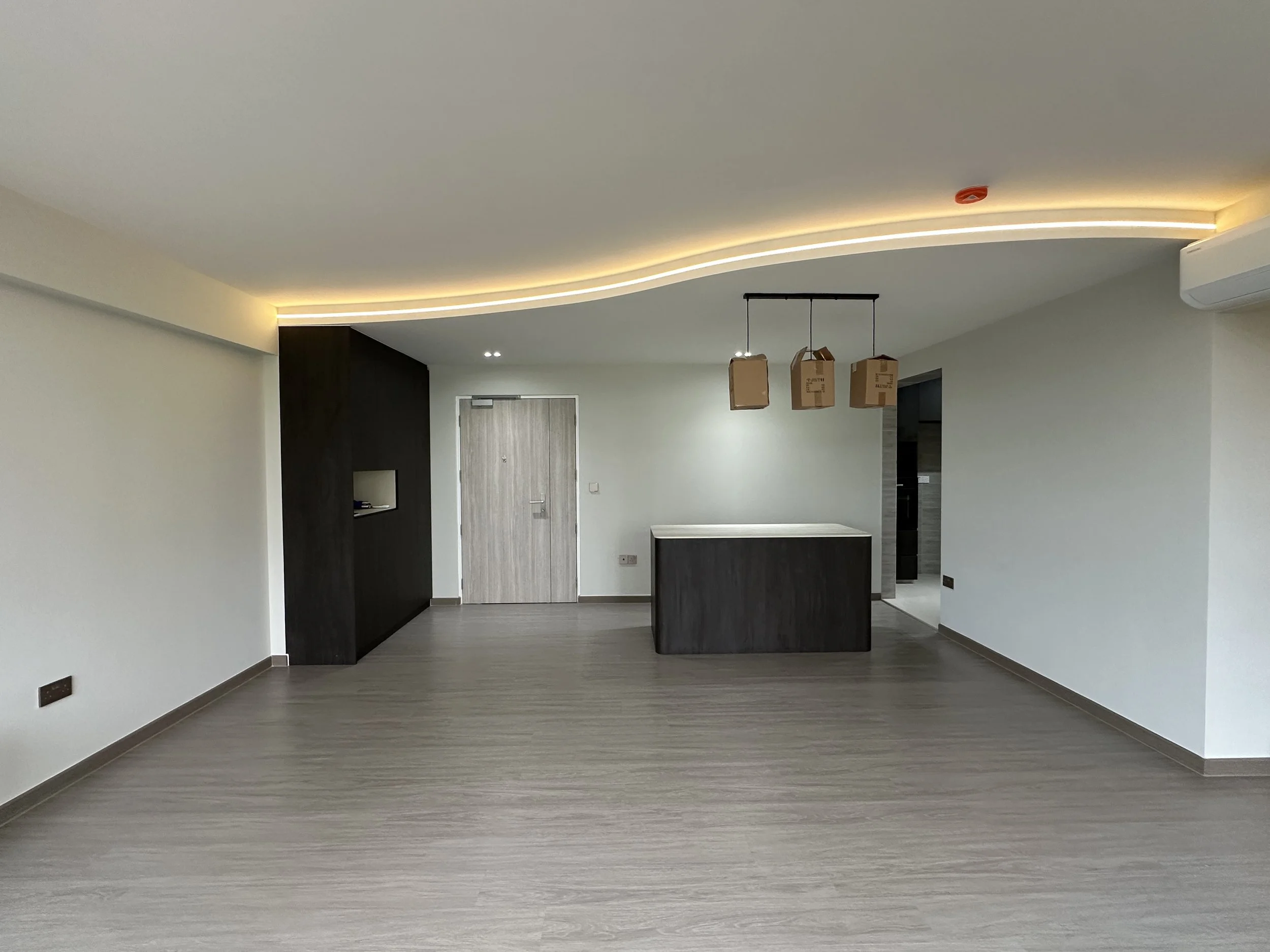 Empty modern living space with wooden flooring, white walls, a dark accent wall, a door, and hanging boxes under a wave-shaped ceiling with LED lighting.