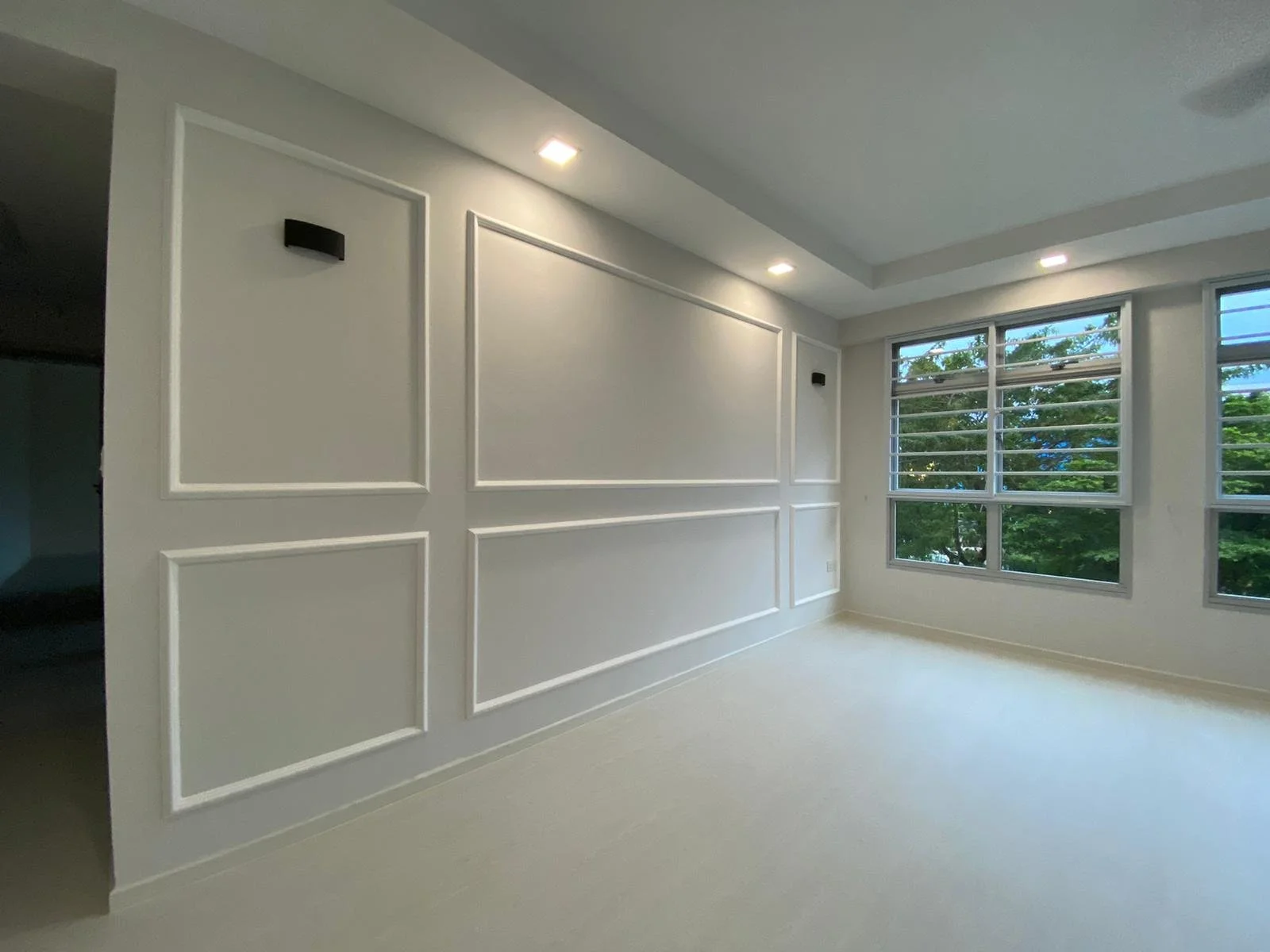 Empty room with large windows and white paneled walls, with partial ceiling lighting