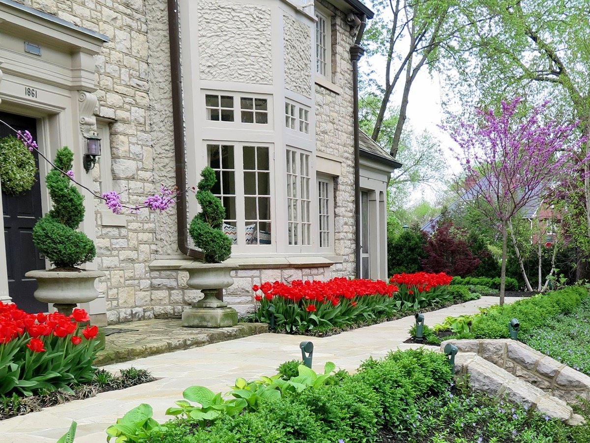Close-up view near front door with two decorative planter pots and swirling shrubs with bright red tulips on either side