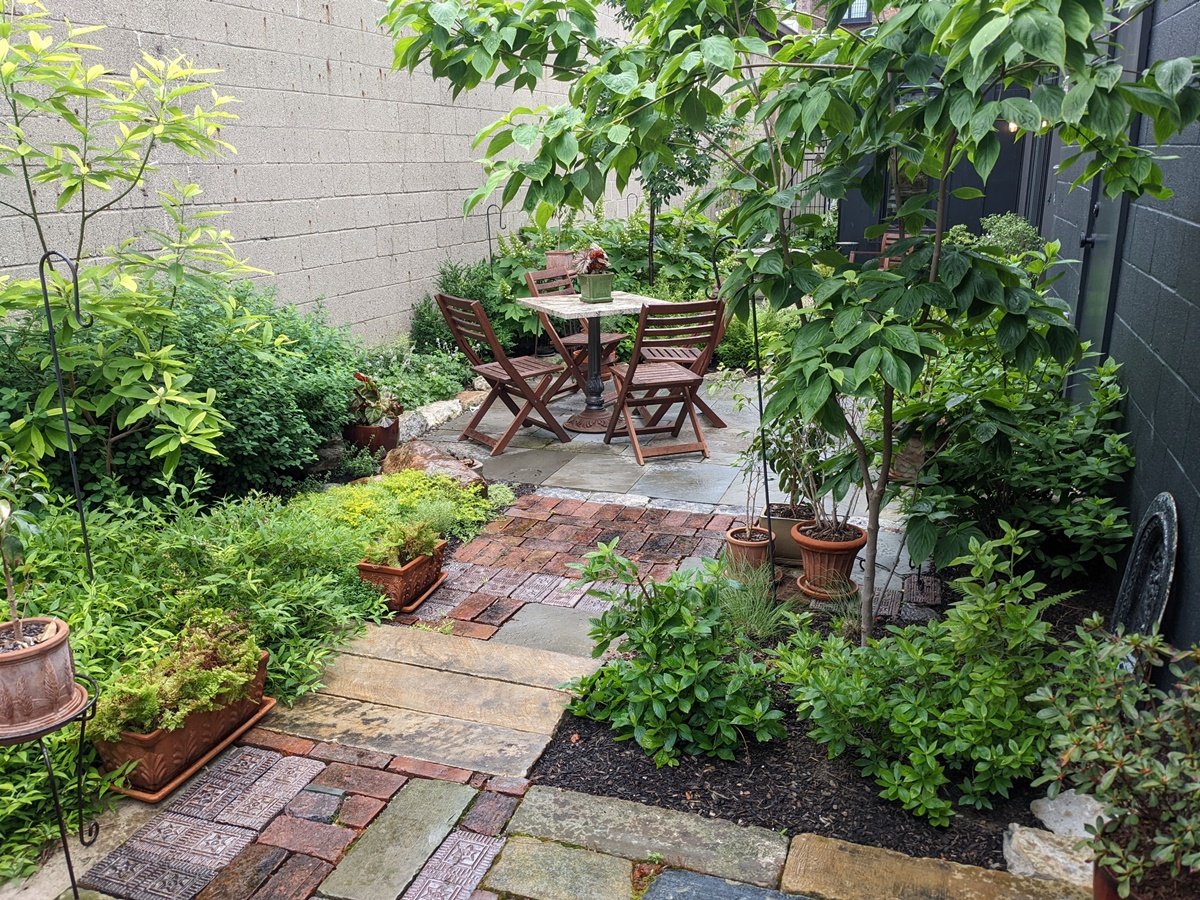 A pathway made of various found materials on the site, such as brick and stone and bluestone, winds through soft-buried plantings to a small patio