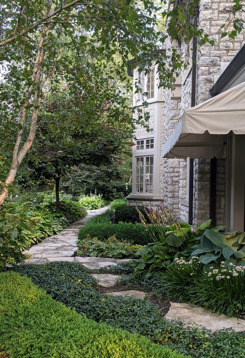 An irregular limestone path winds through vinca ground cover towards the path at the front of the house