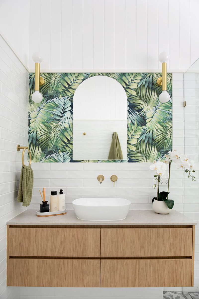 Vanity sink and shower recess with gold tap wear and tropical wallpaper and arch mirror on the splash back. Interior design by Marilena Baynes, Brisbane.