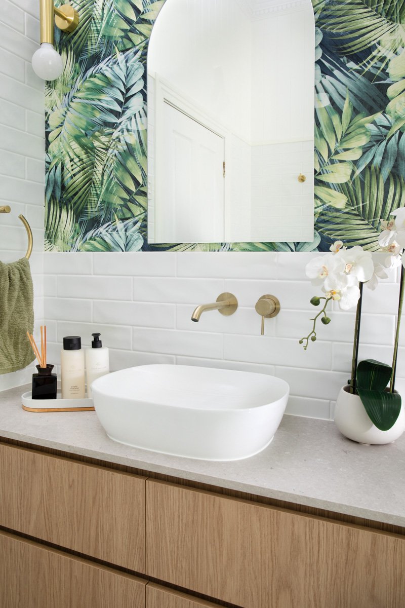 Vanity sink with gold tap wear and tropical wallpaper and arch mirror on the splashback. Interior design by Marilena Baynes, Brisbane.