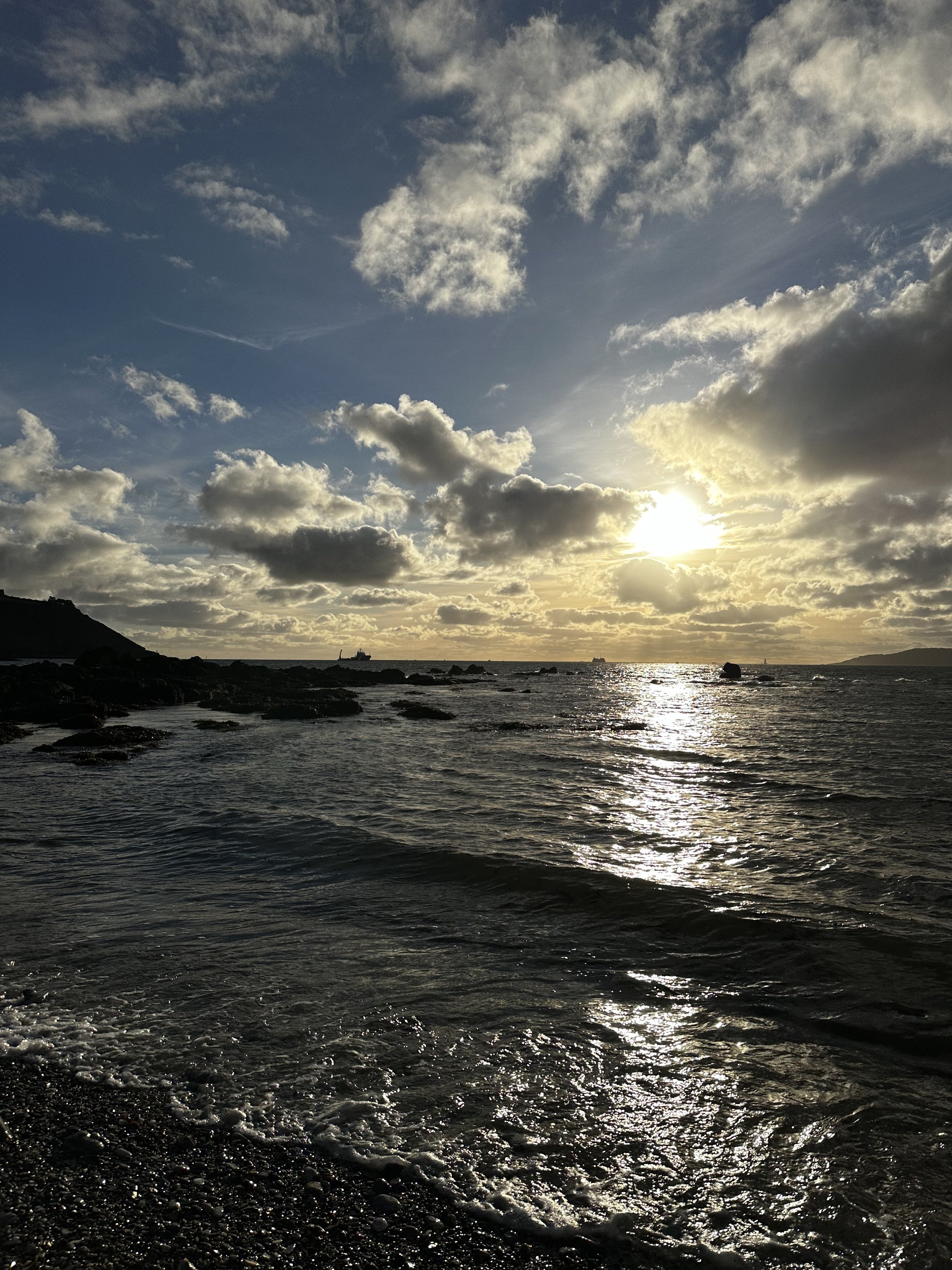 On the shore at Mount Batten, a peninsula in Plymouth Sound. The low winter sun is about to set, the shore and sea are in silhoutte, with the clouds being back lit with a warm orange glow