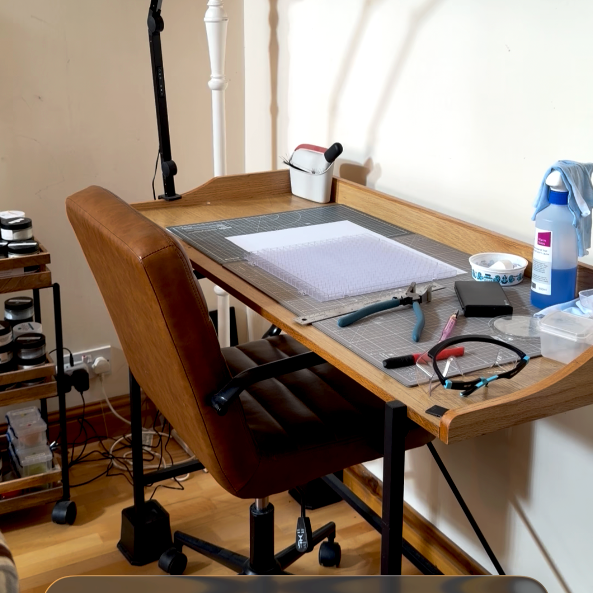 A writing table with a leather wheeled chair pushed underneath it. Glass tools on the table top.