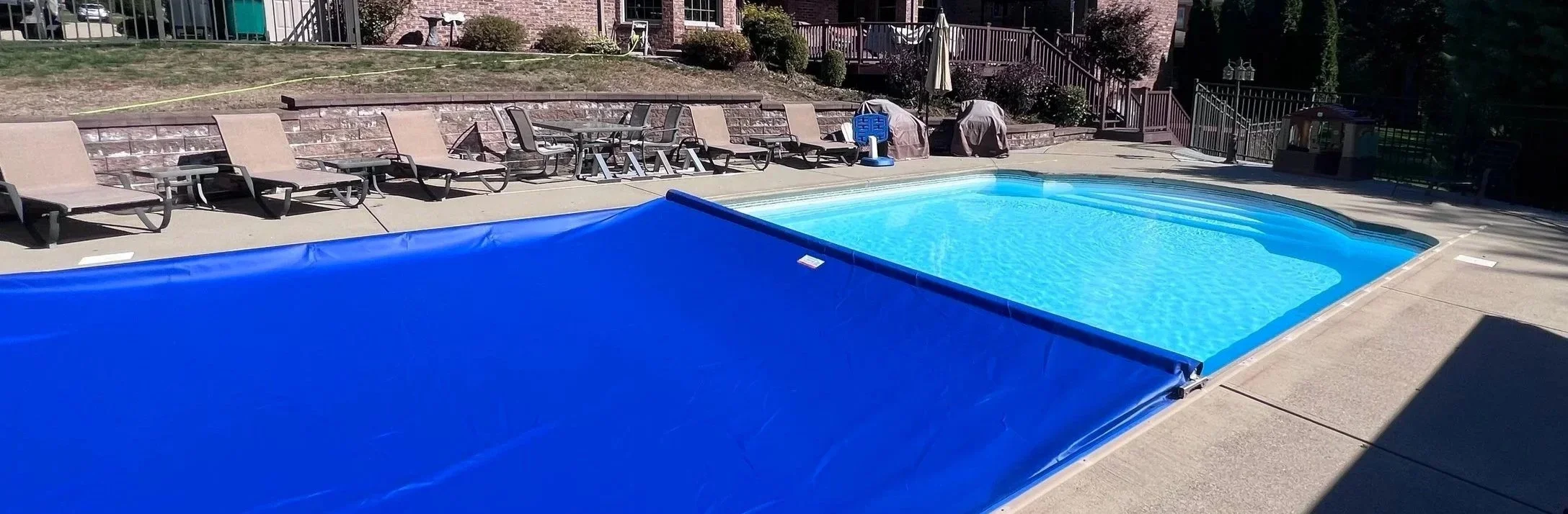 Resort swimming pool with blue cover pulled back, clear blue water, lounge chairs along the poolside, and a decorated brick wall in the background.