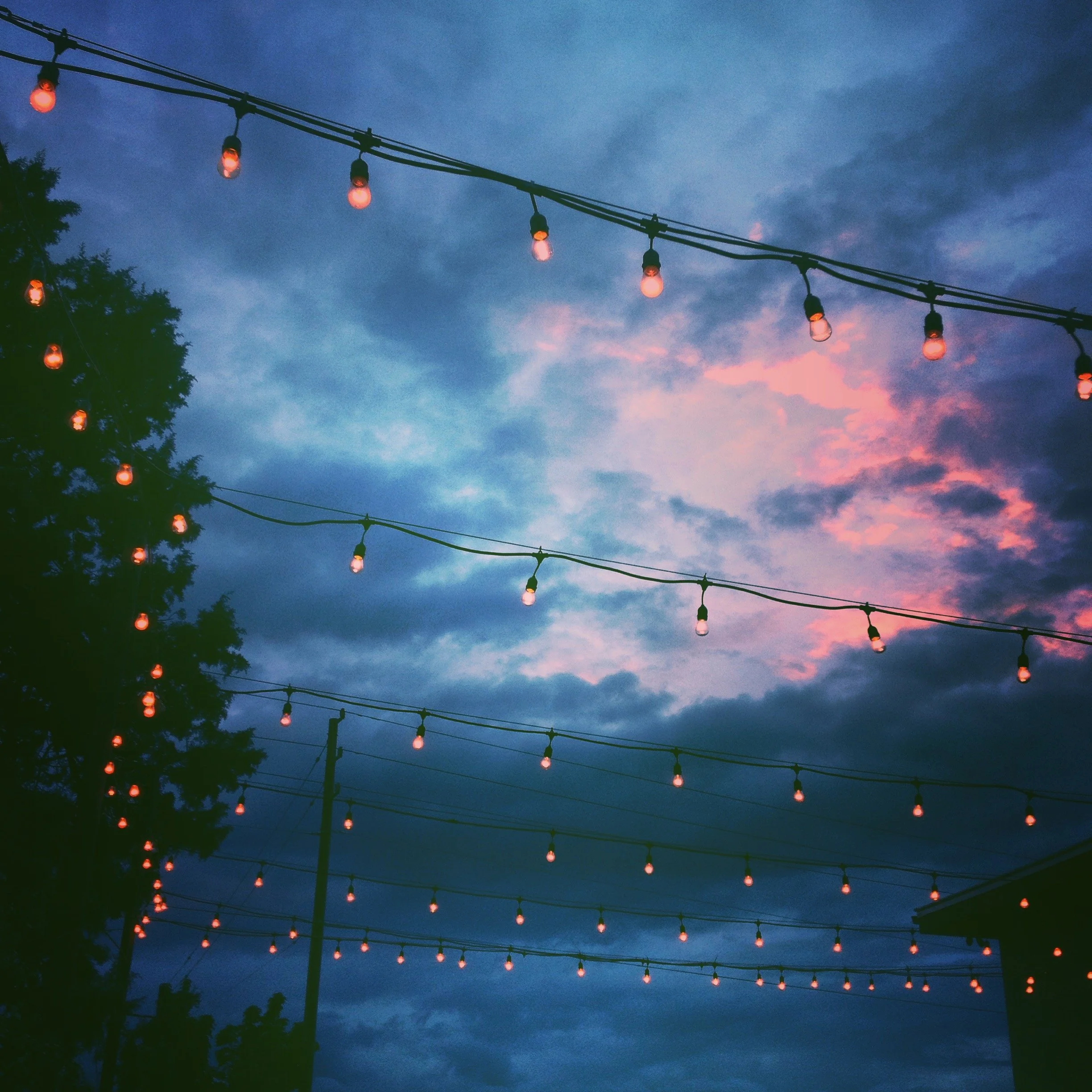 String of hanging outdoor string lights against a pink and blue sky at dusk.