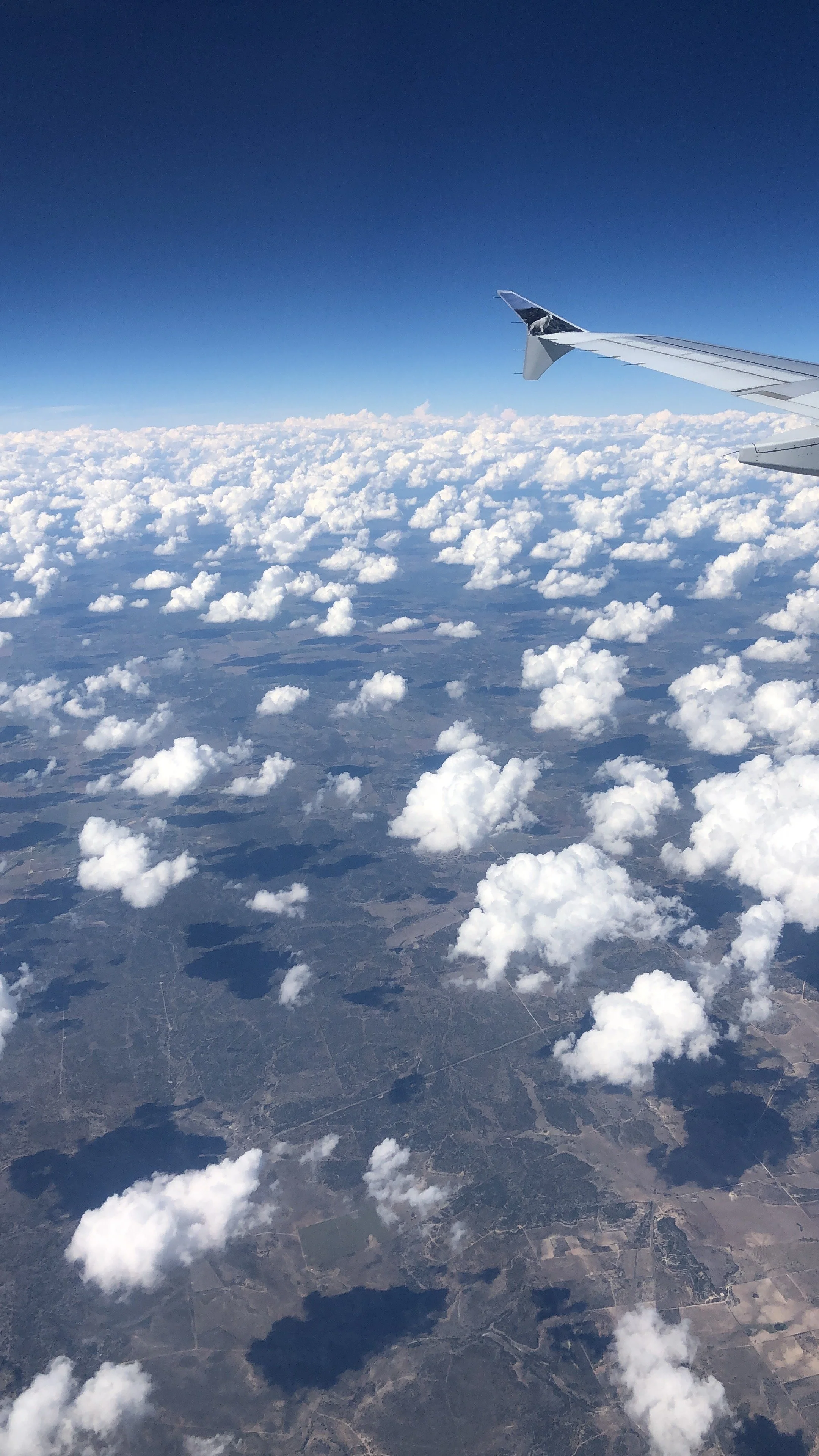 View from an airplane window showing the wingtip, clouds, and landscape below.